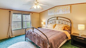 Ein Schlafzimmer mit einem Bett, einem Nachttisch, einem Deckenventilator, einem Fenster mit Vorhängen und einem Gemälde an der Wand.