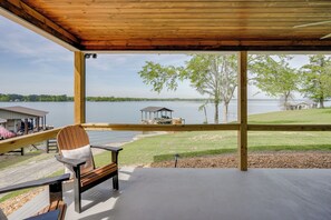 A covered deck with a view of a lake, a wooden chair, and a dock.