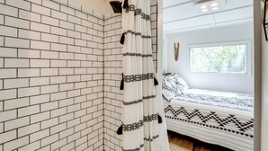 A room with a white brick wall, a bed with patterned bedding, and a window with a view of trees. - Hike On-site: Georgia Tiny Home on Farm Retreat (Lithonia)
