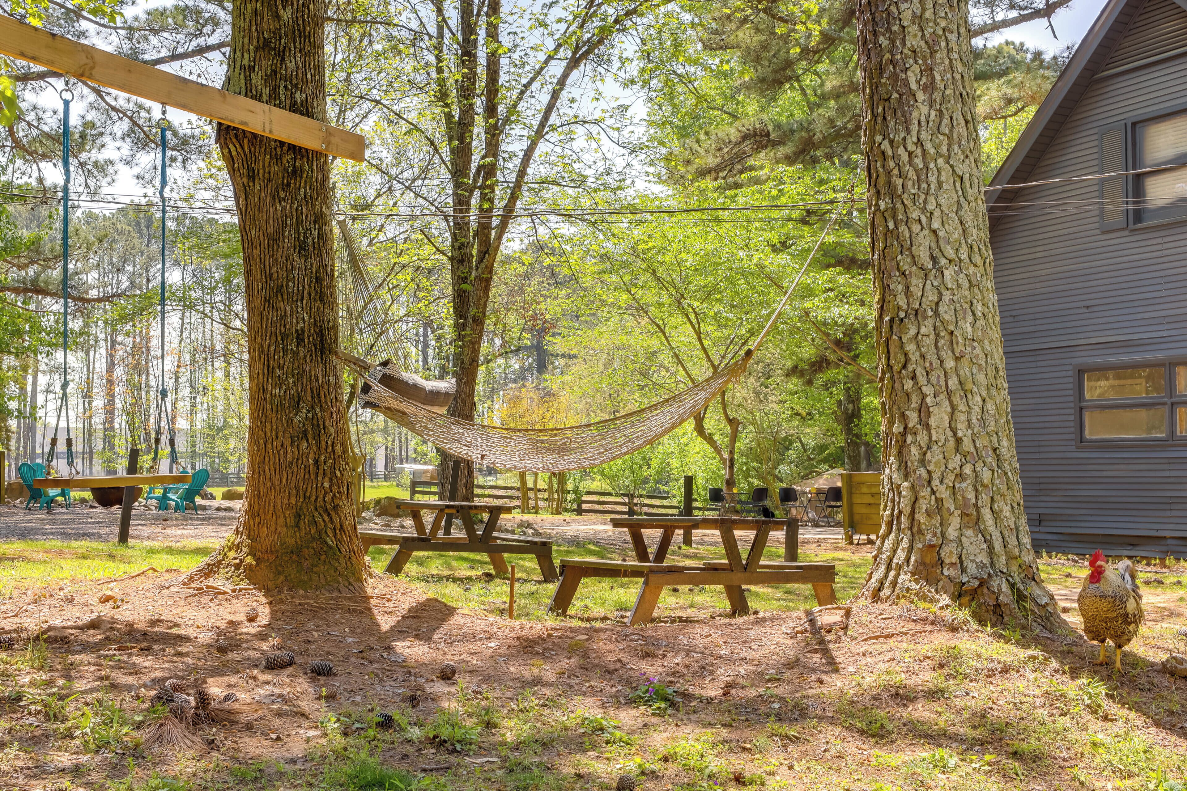 A rustic outdoor area with picnic tables, a hammock, and a wooden structure.