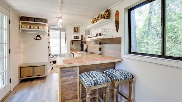 A kitchen with a wooden island, bar stools, and a large window with a forest view. - Hike On-site: Georgia Tiny Home on Farm Retreat (Lithonia)