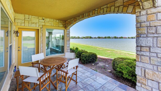 Une terrasse couverte avec une arche en pierre, une table en bois et des chaises, et une vue sur un lac.