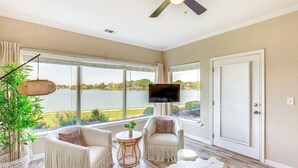 Une pièce spacieuse dotée d’une grande fenêtre donnant sur le lac, d’un ventilateur de plafond et d’un téléviseur à écran plat fixé au mur.