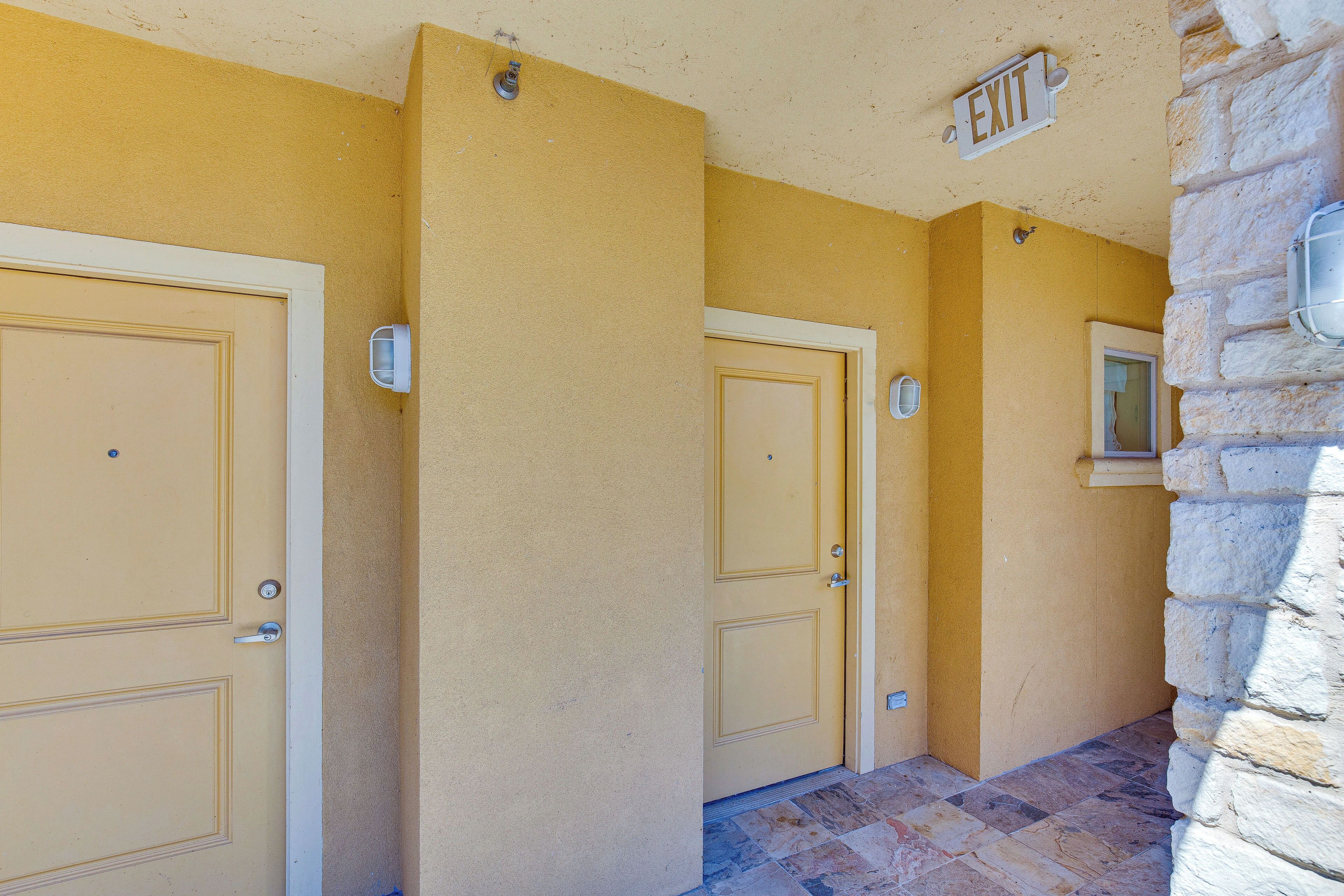 Un pasillo con tres puertas color beige, una pared de piedra a la derecha y una señal de salida sobre la puerta derecha.