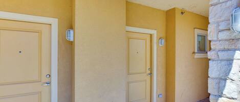 Un pasillo con tres puertas color beige, una pared de piedra a la derecha y una señal de salida sobre la puerta derecha.