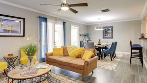 A modern living room with a brown sofa, a coffee table, and a dining area with blue chairs. - Deck & Hiking Trails: Luxe Georgia Farm Retreat (Lithonia)