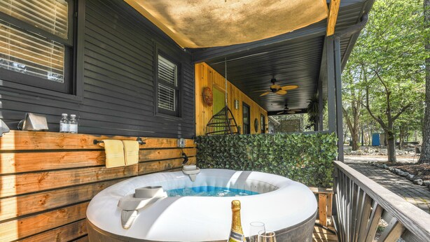 A hot tub with a wooden deck, a bottle of champagne, and two glasses on a table. - Deck & Hiking Trails: Luxe Georgia Farm Retreat (Lithonia)