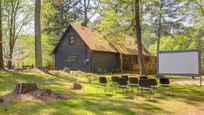 A rustic cabin with a large screen and chairs arranged for an outdoor event. - Deck & Hiking Trails: Luxe Georgia Farm Retreat (Lithonia)