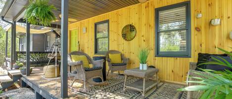 A covered porch with wicker furniture, a ceiling fan, and a wooden wall.