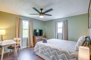 Ein Schlafzimmer mit Bett, Schreibtisch, Stuhl, Fernseher und Deckenventilator.