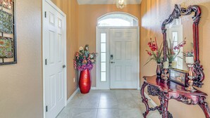 A hallway with a white door, a red vase with flowers, and a mirror on a wooden console table.
