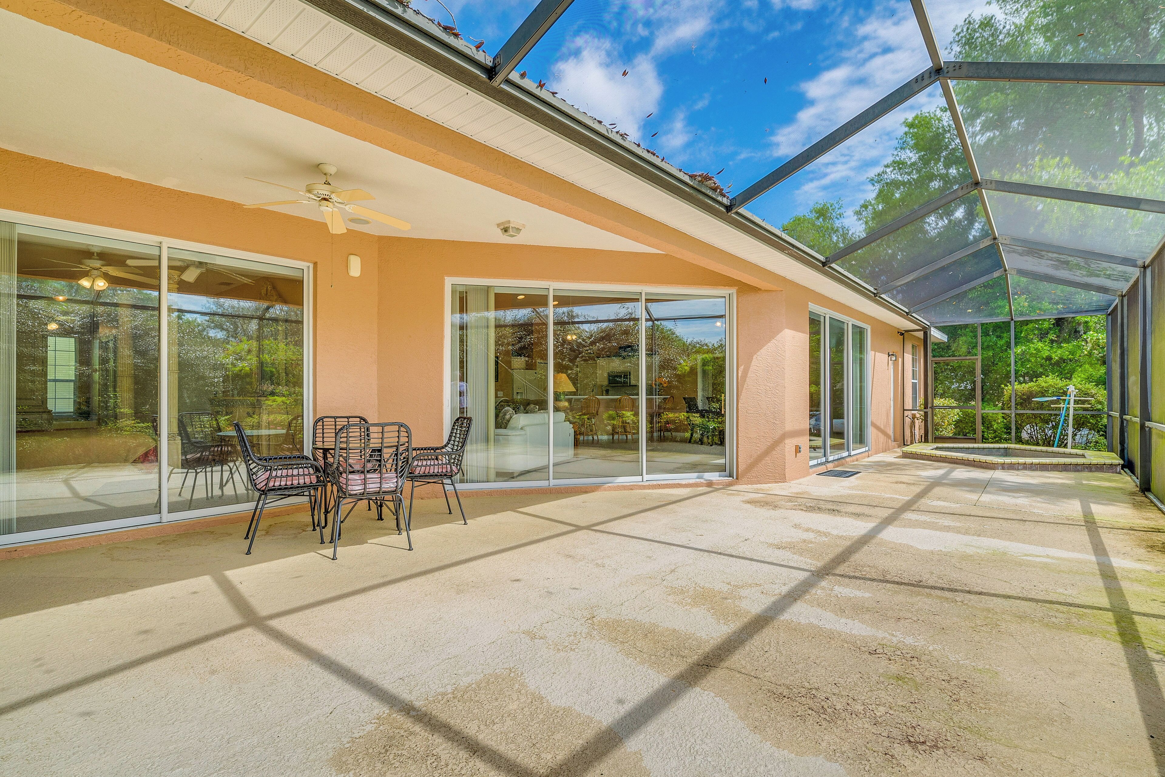 A covered patio with a glass door leading to a living area, a ceiling fan, and a table with chairs.