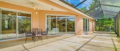 A covered patio with a glass door leading to a living area, a ceiling fan, and a table with chairs.