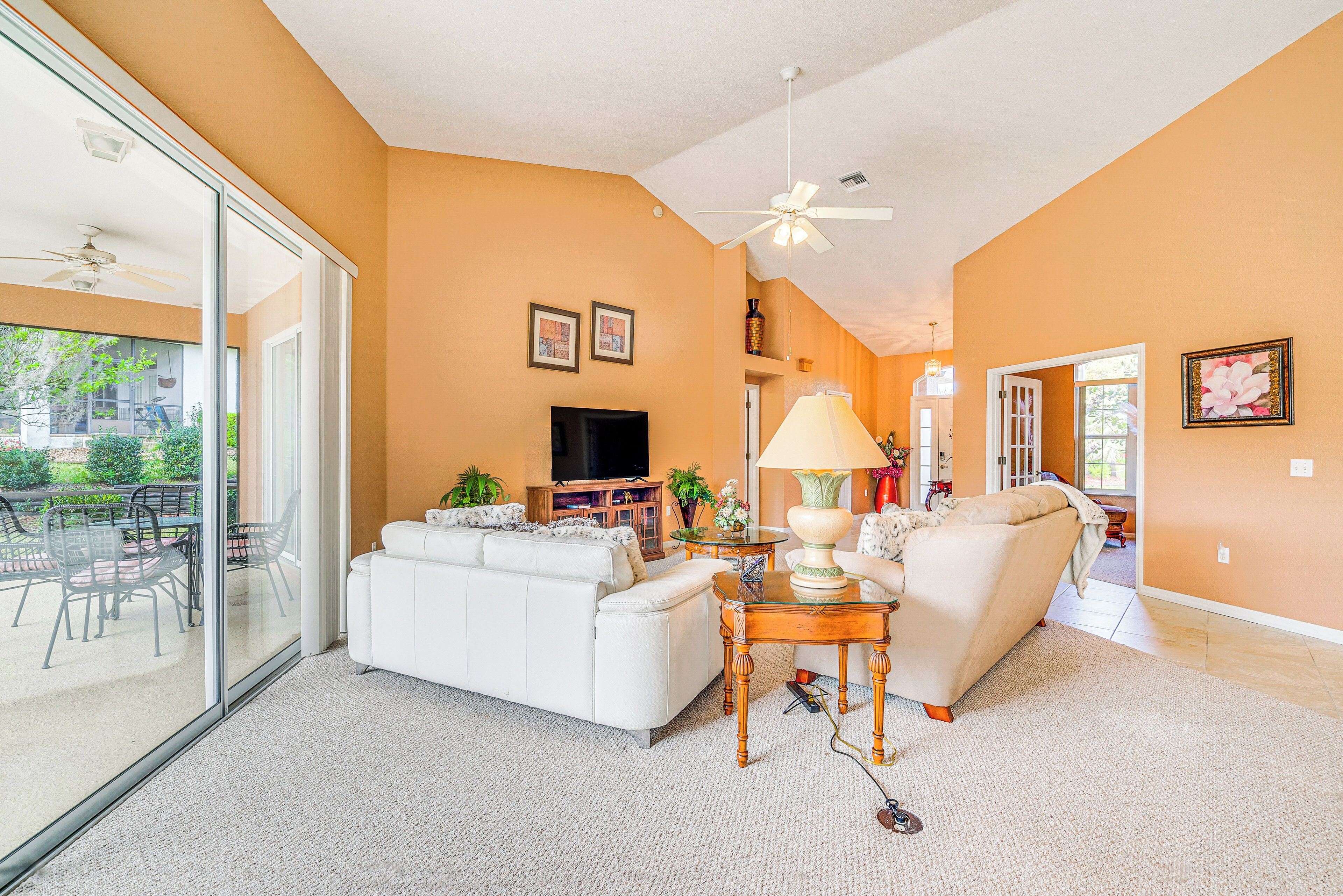 A spacious living room with a white sofa, a coffee table, and a TV. There is a sliding glass door leading to an outdoor patio area.