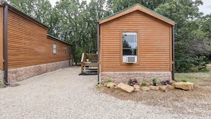 A wooden cabin with a stone foundation, a gravel driveway, and a small garden area with rocks and plants. - Cabin 9 ~ Toronto Lake: Fishing, Swimming & More! 1 Bedroom Cabin by RedAwning (Toronto)