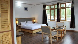 A bedroom with a bed, bedside table, chair, and a window with curtains. - Hotel Leh Residency (Leh)