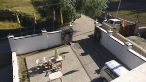 A courtyard with a table and chairs, a small garden, and a white building with a flag. - Hotel Leh Residency (Leh)