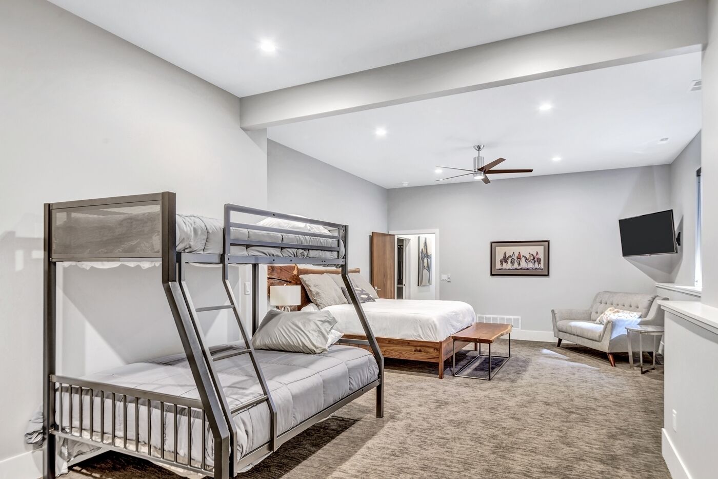 A modern bedroom with a bunk bed, a desk, a chair, a ceiling fan, and a mounted TV.