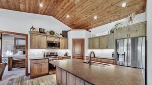 Une cuisine spacieuse avec des meubles en bois, un grand îlot central, des appareils électroménagers en acier inoxydable et un plafond au style rustique.