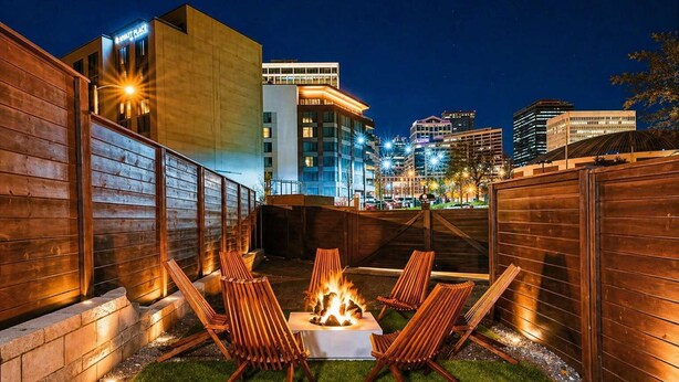 A patio with a fire pit, lounge chairs, and a view of city buildings at night. - Walk 2 Broadway 15 beds! Private Hot Tub & Pool (Nashville)