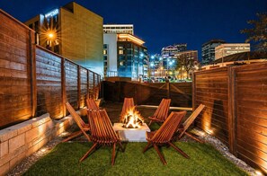 A patio with a fire pit, lounge chairs, and a view of city buildings at night. - Walk 2 Broadway 15 beds! Private Hot Tub & Pool (Nashville)