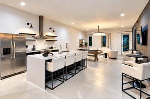 Una cocina moderna con una isla central, electrodomésticos de acero inoxidable y una zona de comedor con mesa de billar.