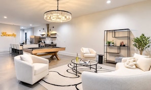 A modern living room with a pool table, a chandelier, and a kitchen in the background. - 14 Beds Walk 2 Broadway Hot Tub Pool Sauna Firepit (Nashville)