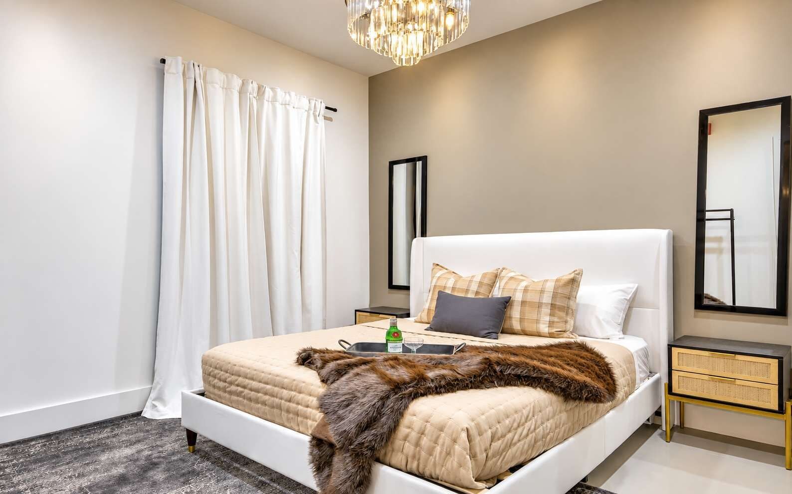 A modern bedroom with a large bed, a bedside table, a mirror, and a chandelier.