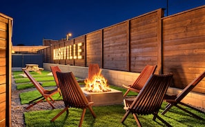 An outdoor seating area with a fire pit and chairs, a wooden wall with 'NASHVILLE' illuminated letters, and a well-maintained lawn. - 14 Beds Walk 2 Broadway Hot Tub Pool Sauna Firepit (Nashville)