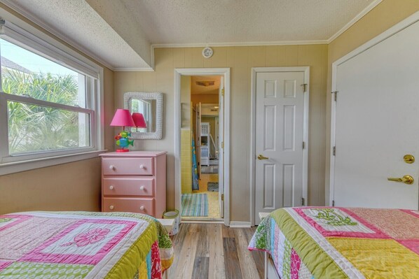 A bedroom with two beds, a dresser, a mirror, and a window.