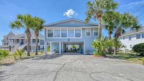A two-story house with a garage entrance, surrounded by palm trees and a clear sky. - Carolina Palms - 5 Bedroom Second Row Beach House (Garden City Beach)