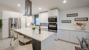 A modern kitchen with white cabinetry, stainless steel appliances, and a central island with seating. - Modern Retreat | Heated Pool, Jacuzzi & Near Beach (Naples)