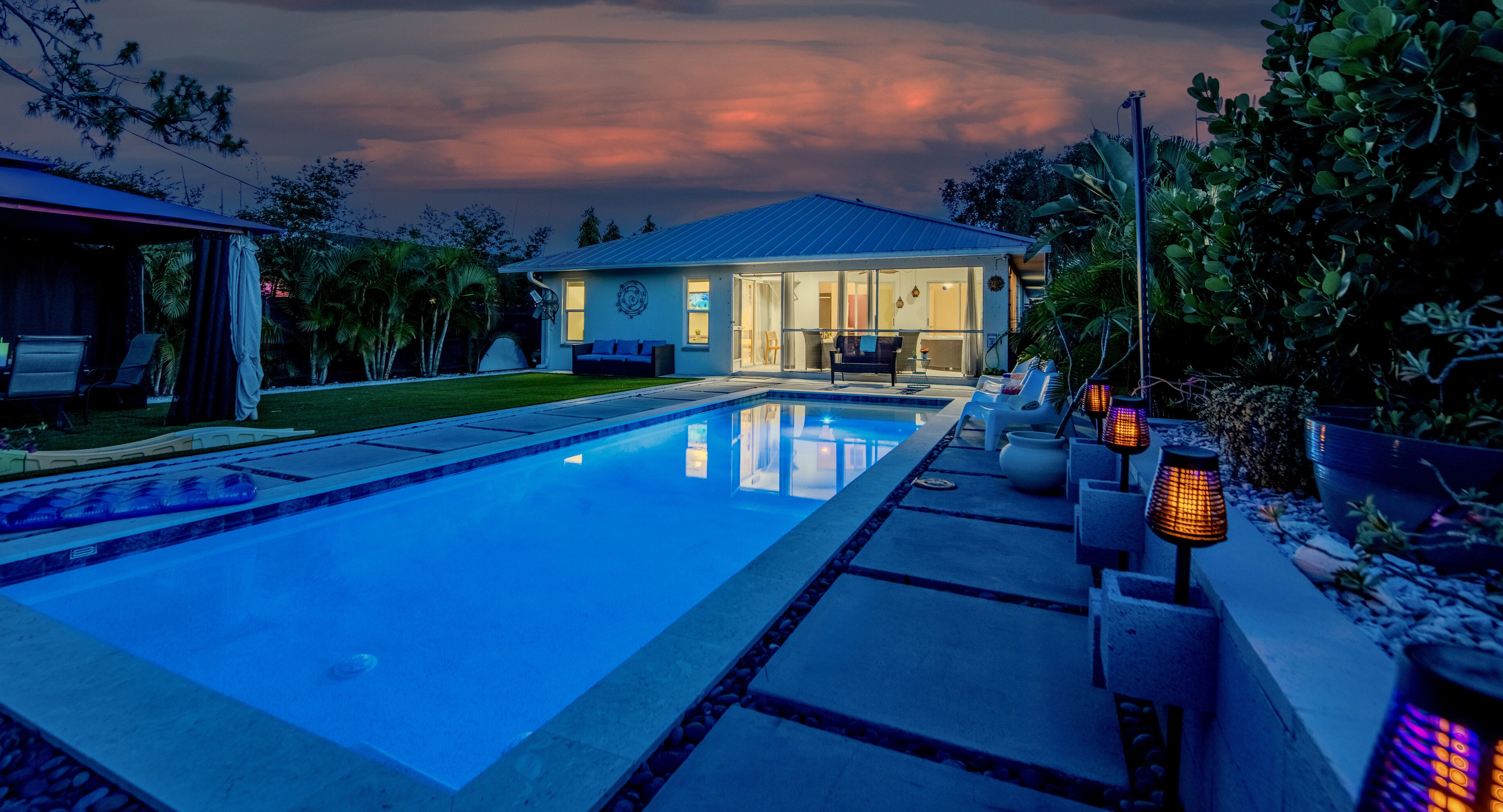 A swimming pool with a house in the background, surrounded by greenery.