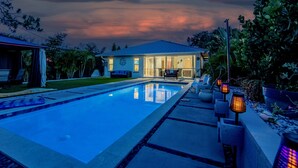 A swimming pool with a house in the background, surrounded by greenery. - Modern Retreat | Heated Pool, Jacuzzi & Near Beach (Naples)