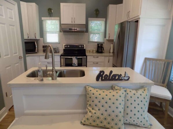 A kitchen with white cabinetry, a stainless steel sink, a stove, and a refrigerator. - The Lantern (Pensacola)