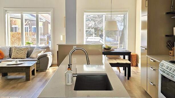 A modern kitchen with a central island, stainless steel appliances, and large windows providing natural light. - Le Valmont | Townhouse 🌾 (Beaupré)