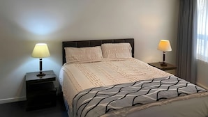 A bedroom with a bed, two bedside tables, and a window with curtains.