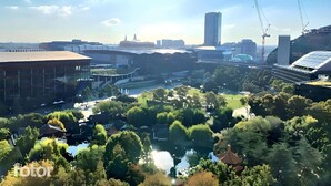 A modern urban landscape with a mix of commercial and residential buildings, a central park area, and a body of water.