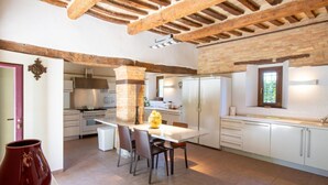 A modern kitchen with exposed wooden beams, white cabinetry, and a central island with chairs. - Villa Gelso: your luxury villa with pool and sauna in Le Marche region (Provincia di)
