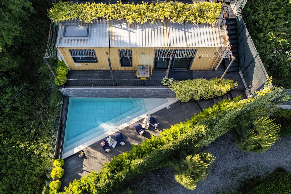 An aerial view of a modern house with a swimming pool, surrounded by lush greenery and a wooden deck.