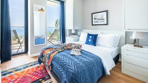 Een moderne hotelkamer met een groot bed, uitzicht op de zee, een balkon met een stoel en een schilderij aan de muur.