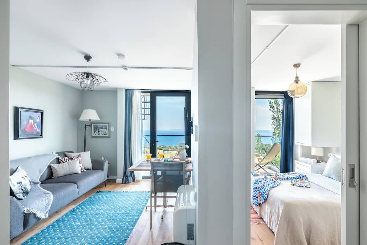 A modern living room with a sofa, a dining table, and a view of the sea.