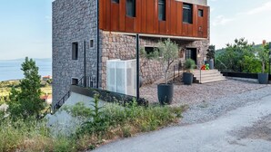 Een modern huis met twee verdiepingen, een stenen gevel en houten bovenverdiepingen, met een trap naar een overdekte veranda.