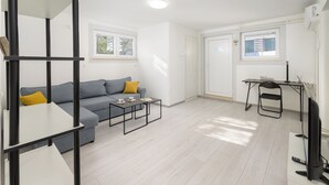Ett modernt vardagsrum med en grå soffa, ett soffbord, en tv och en bokhylla.