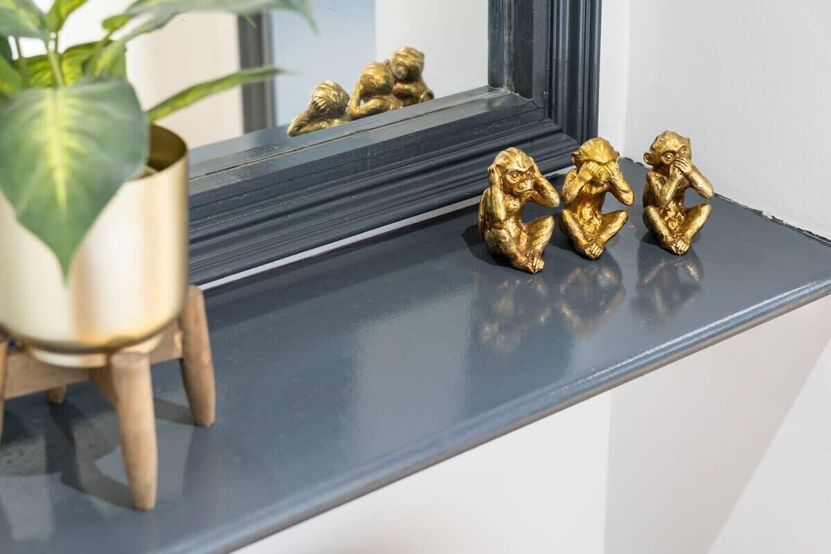 Une étagère avec une plante en pot et trois statuettes dorées.