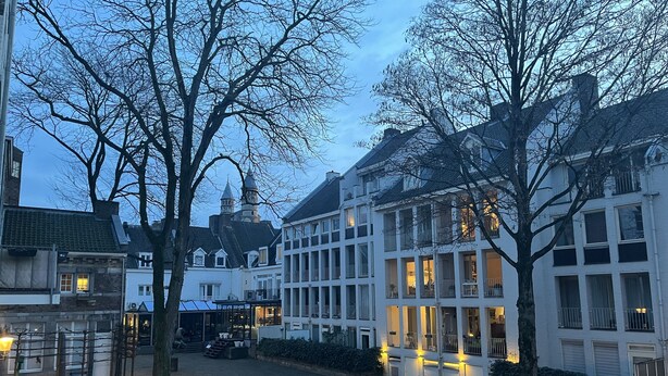 Straatbeeld met traditionele Europese architectuur, waaronder een gebouw met een toren en een ander met meerdere balkons.