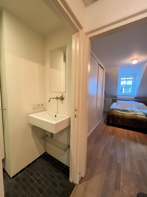 Ein Schlafzimmer mit Bett, Fenster und Badezimmer mit Waschbecken und Spiegel.