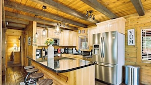 Cocina estilo cabaña de madera con una isla central, taburetes de bar, electrodomésticos de acero inoxidable y un letrero que dice 'YUM'.