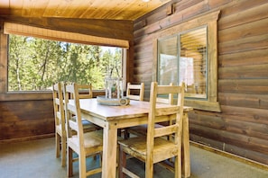 A wooden cabin interior with a dining table, chairs, a large window, and a view of trees. - A real log cabin in the pines with a huge game room and a jacuzzi tub! (Pine)