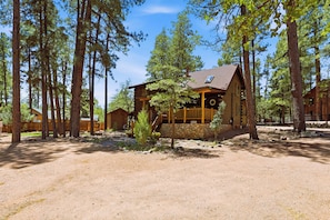 A log cabin with a porch, surrounded by tall pine trees. - A real log cabin in the pines with a huge game room and a jacuzzi tub! (Pine)